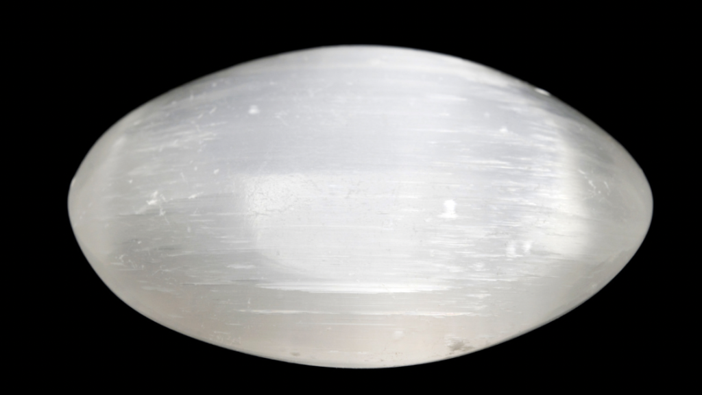 A single polished selenite egg against a black backdrop highlighting its luminous appearance.