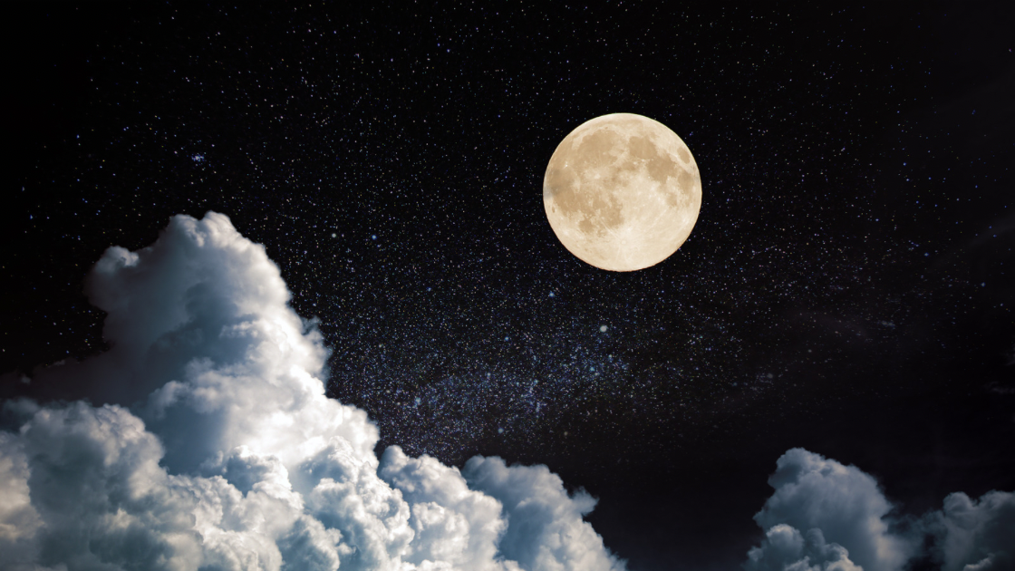 A full moon shining brightly against a starry night sky with fluffy clouds.